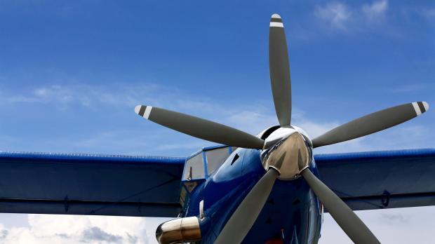 A blue propeller plane sits on a runway in front of a bright blue sky