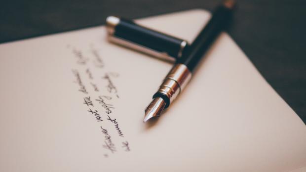 A black fountain pen rests on a piece of paper containing a handwritten note